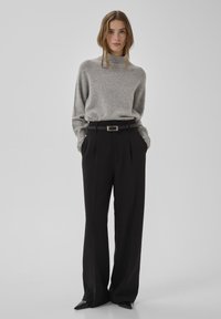 Pelēks adīts džemperis ar augstu apkakli, kopā ar augsta vidukļa melnām biksēm un melnu jostu. Biksēm ir platu kāju dizains.