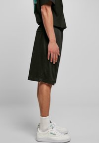 Shorts de sport vert foncé avec une taille élastique, associés à des baskets blanches et des chaussettes côtelées. Design simple, coupe arrivant aux genoux.