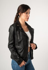 Schwarze Leder-Motorradjacke mit tailliertem Design, Reißverschlusstaschen und Druckknopfkragen. Kombiniert mit einem weißen Oberteil und blauen Jeans.