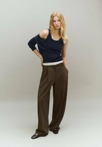 Top de punto azul marino superpuesto sobre una camiseta blanca, combinado con pantalones marrones holgados y calzado oscuro, mostrando una silueta relajada.