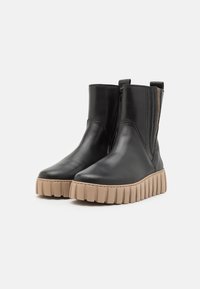 Bottines en cuir noir avec une semelle épaisse beige et des panneaux élastiques sur les côtés pour un enfilage facile. Texture lisse avec un design à bout rond.