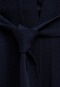 Granatowa dzianina z zapięciem na sznurek, z teksturową powierzchnią i gładkim wykończeniem. Projekt obejmuje styl zawijany z widocznym szwem.