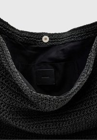 Czarna pleciona torba z teksturowanym, dzianym zewnętrzem, gładką podszewką wewnętrzną oraz metalowym zapięciem na zatrzask z małą kieszonką wewnątrz.