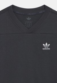 Σκούρο γκρι βαμβακερό T-shirt με σχέδιο σε σχήμα V λαιμόκοψης. Διαθέτει μικρό λευκό κεντημένο λογότυπο Adidas στο αριστερό στήθος. Απαλή, μονόχρωμη υφή.