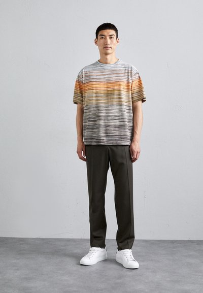 Striped short-sleeve shirt in gray, orange, and yellow hues, with a loose fit. Paired with dark green trousers and white sneakers.