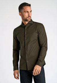 Donkergroene blouse met lange mouwen en een knoopsluiting aan de voorkant, van licht gestructureerde stof, met zwarte knopen. Pasvorm is getailleerd met een puntkraag.