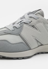 Šedá sportovní bota s kombinací semiše a síťoviny. Design zahrnuje výrazné logo "N" a texturované detaily.