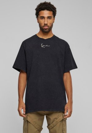 T-shirt noir surdimensionné avec une finition texturée et un logo blanc sur la poitrine, associé à un pantalon cargo beige.