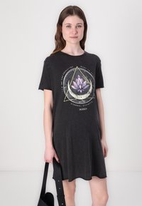Short-sleeve black dress made of soft fabric featuring a lotus graphic and circular text design on the front. Curved hemline.