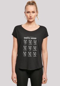 Svart T-skjorte med korte ermer med hvit grafikk som viser ni Darth Vader-ansikter, hver merket med forskjellige følelser. Rundet kantdesign.