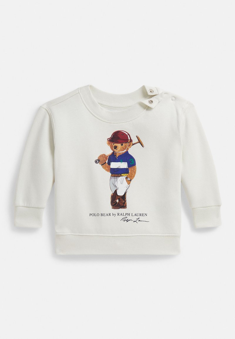 Krem dukserica od meke tkanine, s šarenom ilustracijom medvjeda u polo majici. Dizajnirana s kopčama na ramenu.