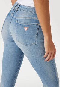 Jeans de mezclilla en azul claro con una cintura alta, un diseño ajustado y un pequeño logo triangular rojo y blanco en el bolsillo trasero.
