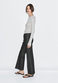 Lichtgrijze aansluitende blouse met lange mouwen, gecombineerd met donkere, grijze wijde broek en zwarte slippers; minimalistisch ontwerp met een elegante silhouet.