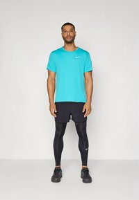 T-shirt Nike turquesa, mangas curtas, mistura de algodão; calções de corrida pretos; leggings pretos compridos, textura suave; ténis desportivos pretos.