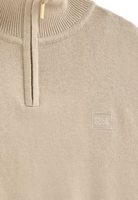 Pull en maille beige clair avec un col partiel zippé et une petite pièce carrée avec le logo "POLO CLUB" sur la poitrine.