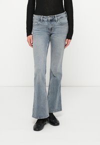 Jean évasé bleu clair en denim, doté d'une fermeture à bouton et zip, de cinq poches et d'une finition délavée. Le tissu principal possède une texture douce.