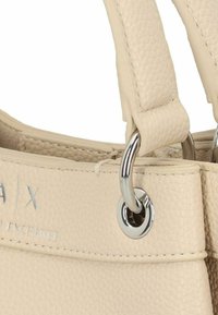 Borsa a tracolla in finta pelle beige con superficie testurizzata, accessori in metallo color argento e manici larghi attaccati tramite anelli metallici. Logo impresso sul lato.
