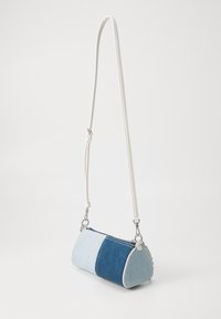 Denim crossbody bag with a cylindrical shape, featuring light and dark blue panels, white strap, silver hardware, and zipper closure.