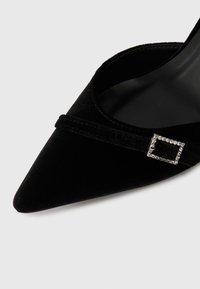 Μαύρο βελούδινο παπούτσι με αιχμηρή μύτη, λεπτή λωρίδα και τετραγωνική διακόσμηση με μικρές διάφανες ρουμπίνες. Λείος μαύρος εσωτερικός φινίρισμα.