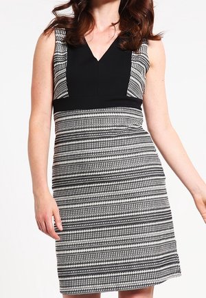 Woman wearing sleeveless black and white patterned knee-length dress with black V-neck bodice and patterned skirt.