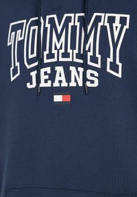 Felpa blu navy con testo bianco "TOMMY JEANS" e un piccolo logo rettangolare in rosso, bianco e blu navy sotto il testo.