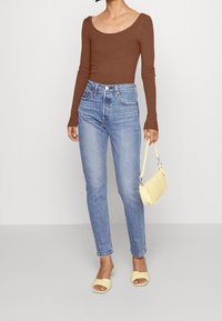 Brun ribbad långärmad topp, ljusblå högmidjade jeans, gul handväska och gula slidesandaler. Enkel design, åtsittande silhuett.