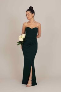 Vestido de noite verde com decote coração, alças finas e fenda lateral. Modelo segura rosas brancas, usando saltos prateados com tiras e brincos.