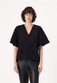 Black embroidered blouse with a V-neck, short puff sleeves, and intricate cut-out floral patterns. Paired with black leather pants.