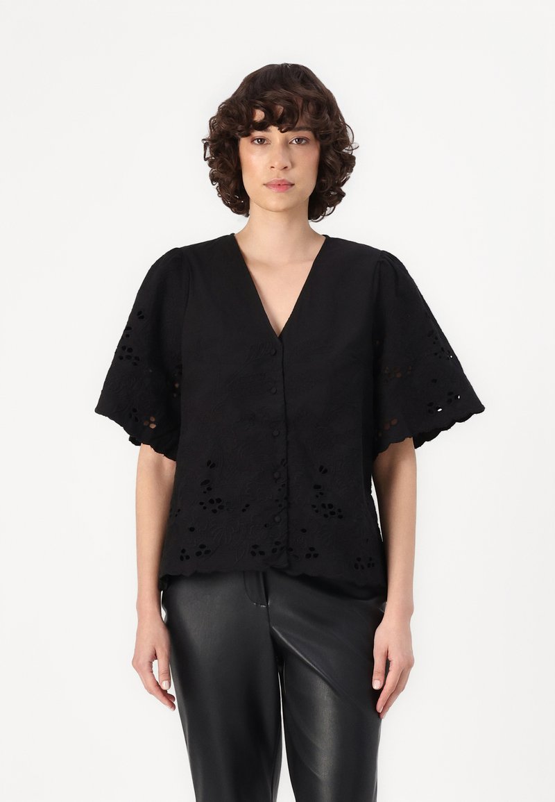 Black embroidered blouse with a V-neck, short puff sleeves, and intricate cut-out floral patterns. Paired with black leather pants.