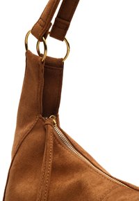 Bolso de ante marrón con cremallera dorada y dos anillos metálicos dorados que sujetan la correa al cuerpo del bolso, sobre un fondo blanco.