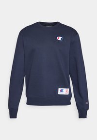 Sudadera azul marino con cuello redondo, puños y dobladillo acanalados. Presenta un parche con logo rojo y blanco en el pecho y una pequeña etiqueta en la cintura.