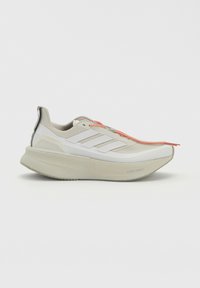 Λευκό και μπεζ αθλητικό παπούτσι Adidas με παχιά σόλα, τρεις λευκές πλαϊνές ρίγες και κόκκινες και λευκές κορδόνια, εμφανίζεται από το πλάι σε λευκό φόντο.