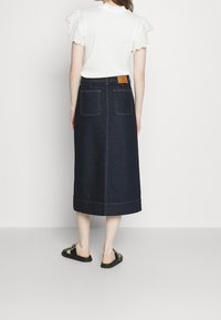 Mörkblå denim midi kjol med två bakfickor, synlig sömnad och rundad fåll. Matchas med en vit topp och svarta sandaler.