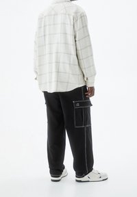 Camisa de cuadros beige con corte amplio, combinada con pantalones cargo negros con costuras blancas y bolsillos laterales, complementados con zapatillas blancas.