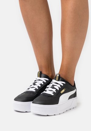 Baskets noir et blanc avec une tige en cuir texturé et une semelle blanche épaisse. Elles présentent des lacets blancs et des accents de marque dorés.