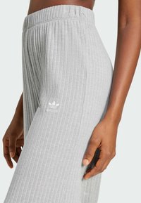 Ljusgrå ribbade joggingsbyxor med elastiskt midjeband. Har en liten vit adidas-logotyp på vänster lår. Slät textur.