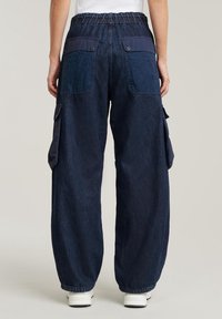 Tummansinisiä cargo-housuja, joissa on rento leikkaus, joustava vyötärö, kaksi takataskua ja sivutaskut. Valmistettu denimistä, jossa on teksturoitu pinta.