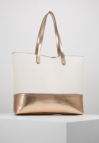 Bolso tote de cuero blanco con un fondo metálico dorado rosa, correas de hombro planas y una textura suave con un diseño minimalista.