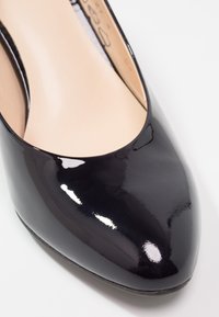 Chaussure plate à bout pointu en cuir verni noir avec intérieur beige et finition lisse et brillante sur fond blanc.
