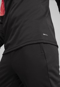 Schwarzes Sportshirt aus strukturiertem Material mit rotem Design und sichtbar eingesticktem "DRYCELL"-Logo am unteren Rand nahe dem Saum.