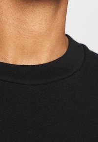 Svart t-shirt med rund halsringning i ett mjukt, strukturerat material. Plagget har en slät halsringning och en minimalistisk design utan dekorationer.