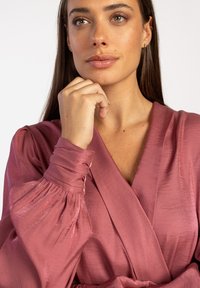 Roze gekleurde wikkelblouse met een V-hals, pofmouwen en een gladde, iets glanzende textuur. Beschikt over een ingestikte taille.