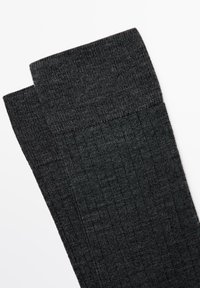 Svarta ribbade strumpor med ett texturerat stickat mönster, med ett fast band upptill, visade sida vid sida mot en vit bakgrund.