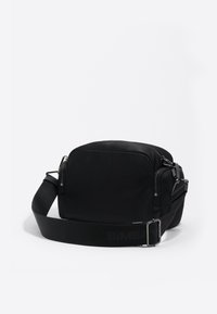 Kompaktná čierna crossbody taška s nastaviteľným širokým popruhom a viacerými zipsovými vreckami na bielom pozadí.