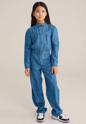 Denim jumpsuit met lange mouwen, kraag, elastische taille en twee voorzakken. Gemaakt met zwarte en witte sneakers.