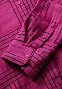 Camicia fucsia con righe nere a contrasto e colletto button-down. Il tessuto ha un aspetto texture, con bottoni rosa ai polsini.