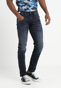 Mörkblå denimjeans med slim-fit, som har fem fickor och subtila slitningar. Matchas med svarta högre sneakers.