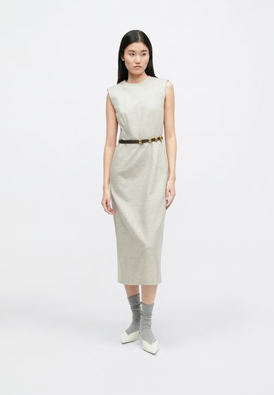 Αμάνικο μπεζ μίντι φόρεμα με δομημένη σιλουέτα, τονισμένο με καφέ ζώνη που διαθέτει χρυσές λεπτομέρειες. Το μοντέλο συνδύασε με γκρίζες κάλτσες και λευκά παπούτσια.