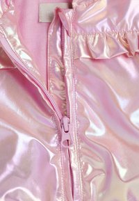 Veste rose brillante avec une fermeture éclair partiellement ouverte, dévoilant un tissu intérieur rose doux et un bord froncé près de l'épaule.