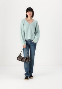 Pull en maille oversize bleu clair avec un col en V, associé à un jean bleu et un petit sac à main marron. Le modèle porte des baskets noires.